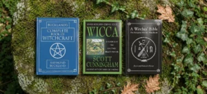 Three classic Wicca and witchcraft hardbacks laid side by side on a moss-covered rock, framed by ivy and fallen oak leaves.