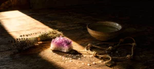 An amethyst cluster, dried lavender, scattered salt and a knotted cord on a wooden table, half lit by a shaft of daylight and half in shadow.